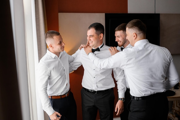 Side view of handsome guys in formal clothes standing and hugging bridegroom smiling and greeting his during wedding day in hotel room