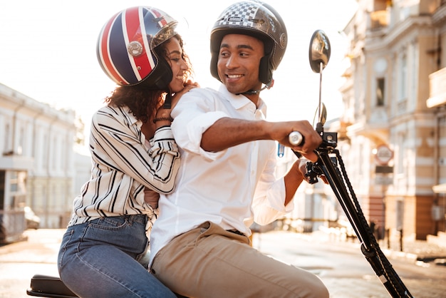 Вид сбоку счастливой африканской пары едет на современном мотоцикле по улице