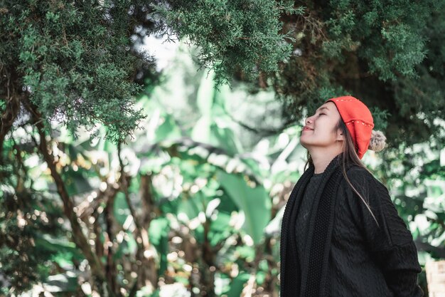 Side view of Happy Asian young woman in winter costume relaxing breathing fresh air outdoors at the forest with copy space Vacation and travel concept