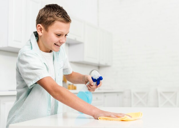 Side view of happy boy cleaning table with rag