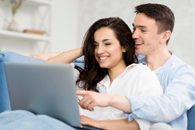 Side view of happy couple on sofa looking at laptop