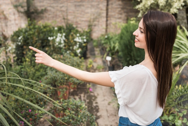 Side view of a happy female gardener pointing towards something in greenhouse