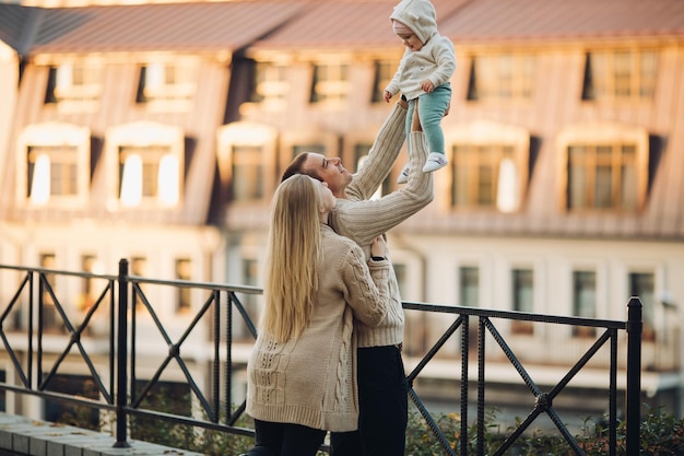 Side view of happy husband and wife with their lovely child Handsome man holding little baby and beautiful woman hugging him from back Young family in casual clothes walking together in sunny day