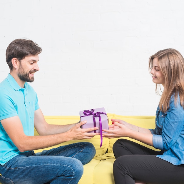 Foto gratuita vista laterale di un uomo felice che si siede sul divano dando il regalo di san valentino alla sua ragazza