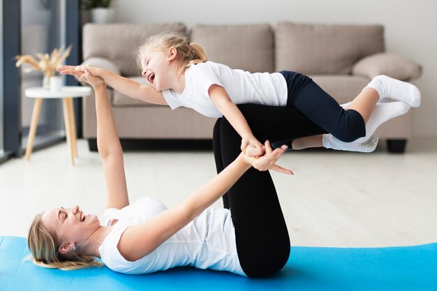 Side view of happy mother and daughter at home on yoga mat