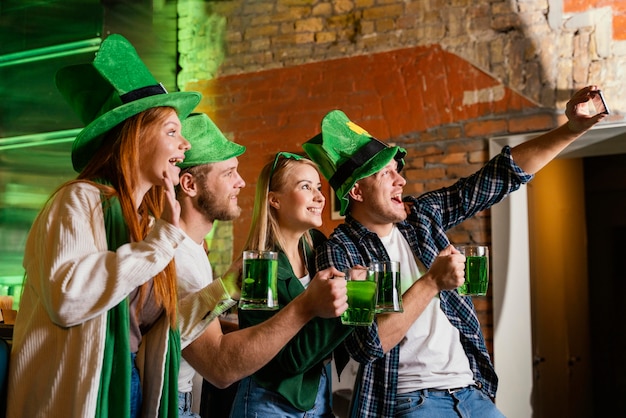 Vista laterale di persone felici che celebrano st. patrick's day e prendendo selfie