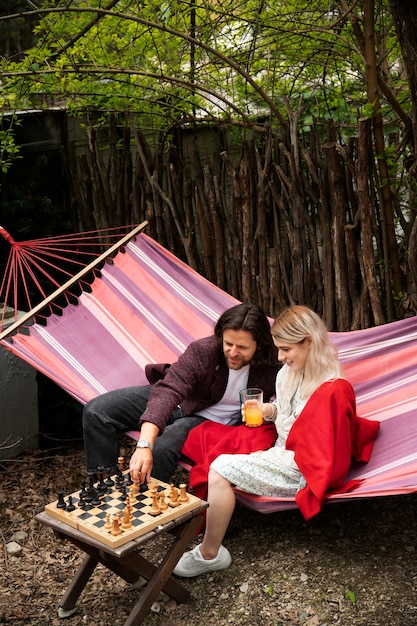 Free photo side view happy people playing chess in hammock