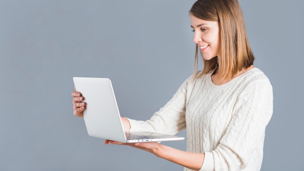 灰色の背景にノートパソコンを持っている幸せな女性の側面図