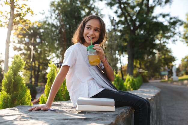 Side view of happy young brunette girl sitting outdoors