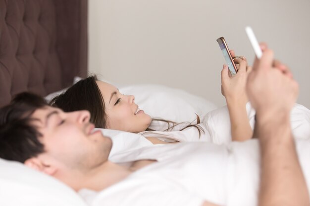 スマートフォンを使用してベッドで幸せな若いカップルの側面図
