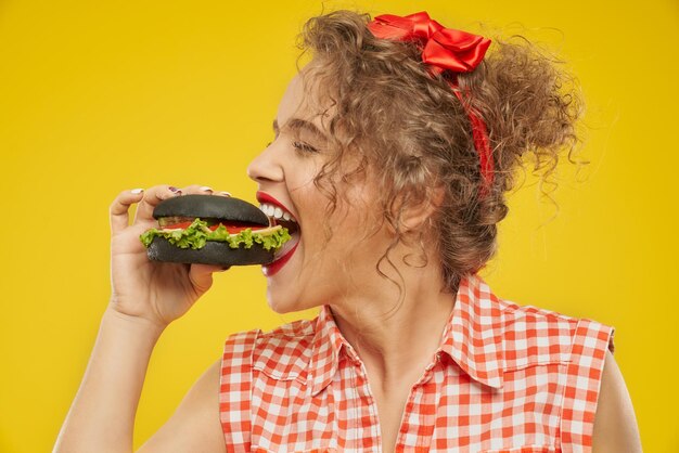 Side view of happy young girl trying to eat black burger