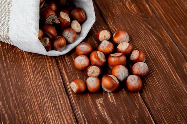 Side view of hazelnuts in shell scattered from a sack on wooden background