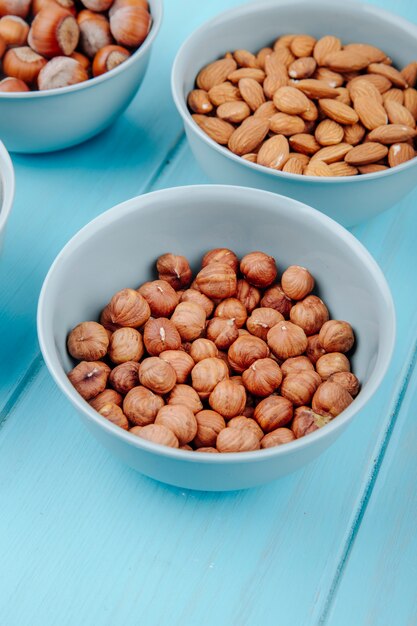 Side view of hazelnuts with almond in bowls on blue background