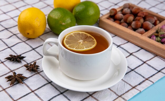 Side view of hazelnuts with walnuts and a cup of tea with lemon on a checkered towel