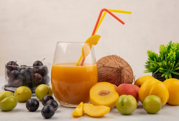 Side view of healthyfresh and colorful fruits such as sloes on a glass bowlpeachescoconut with fresh peach juice on a glass on a white background