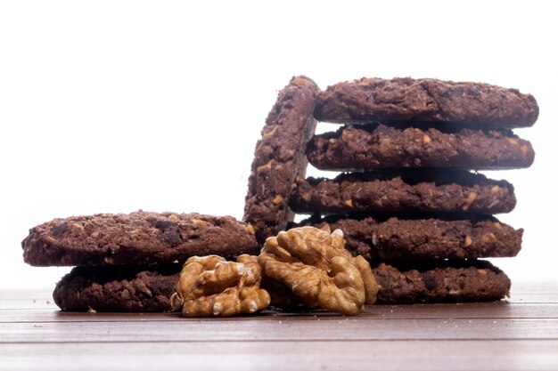 Вид сбоку кучи шоколадного печенья с хлопьями орехов и какао на столе
