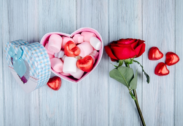 핑크 마쉬 멜 로우와 초콜릿 사탕 가득 빨간 심 혼 및 회색 나무 테이블에 빨간 장미 꽃으로 가득 하트 모양의 선물 상자의 측면보기