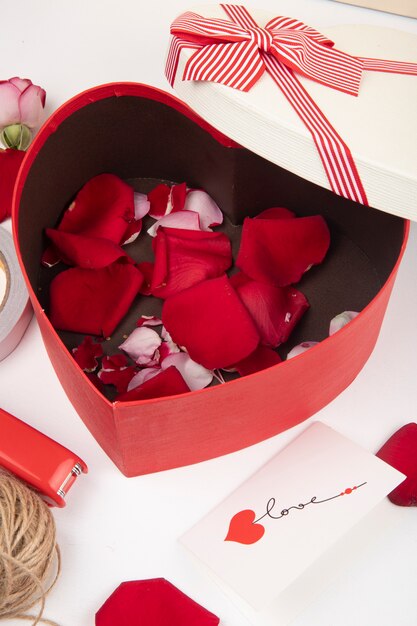 심장 모양의 선물 상자의 측면보기 흰색 배경에 빨간 장미 꽃잎으로 가득