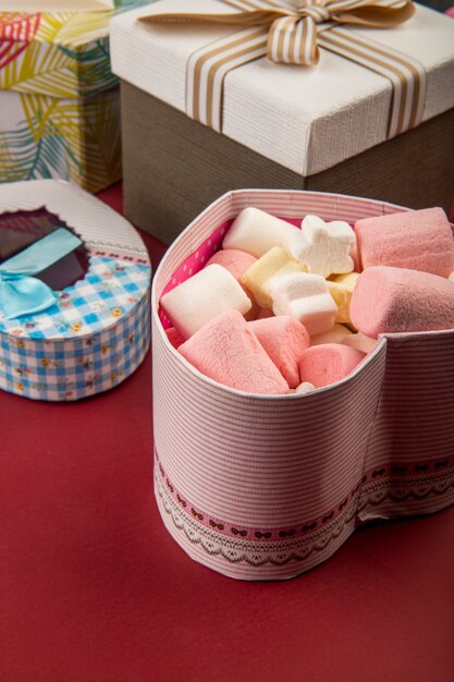 Side view of a heart shaped present box filled with marshmallow on red table