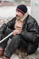 Free photo side view of homeless man holding a cane