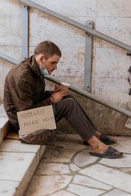Free photo side view of homeless man holding cup and help sign