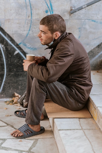 Side view of homeless man holding cup on stairs