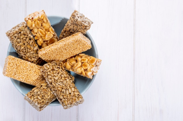 Side view of honey bars with peanuts sesame and sunflower seeds in a bowl on white