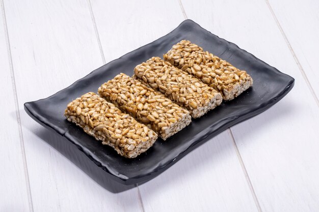 Free photo side view of honey bars with sunflower seeds on a black platter on rustic