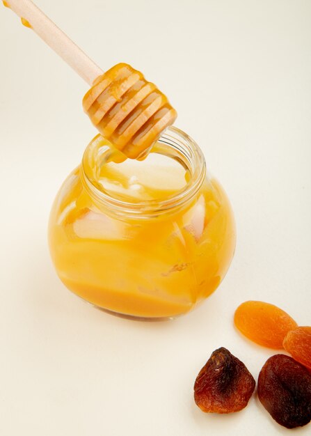 Side view of honey in glass jar with raisins on white table