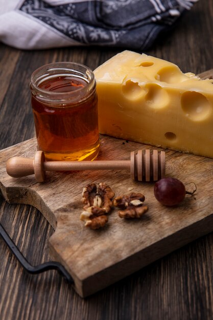 Вид сбоку мед в банке с сыром и грецкими орехами с виноградом на подставке