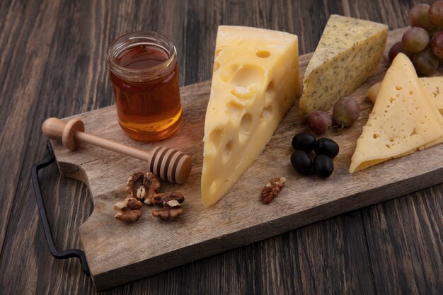 Free photo side view honey in a jar with different cheeses and walnuts with grapes on a stand