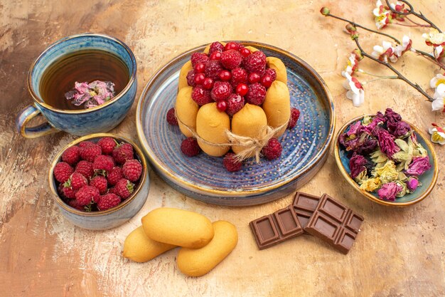 Боковой вид мягкого торта горячего травяного чая с фруктами и шоколадными батончиками на столе смешанного цвета