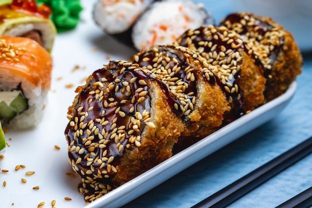 Side view hot roll deep fried sushi roll with teriyaki sauce and sesame seeds on a plate