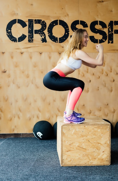 Free photo side view image of fit young woman doing a box jump exercise. muscular woman doing a box squat at the gym