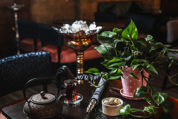 Вид сбоку железный чайник со стаканом чая и растением в горшке на столе