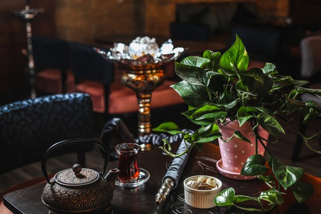 Side view iron teapot with a glass of tea and a potted plant on the table