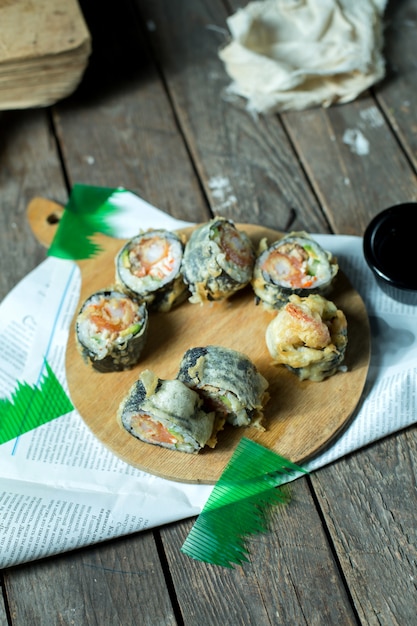 Side view of japanese traditional food tempura sushi maki served with ginger and soy sauce on wooden board