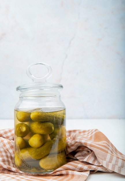 Side view of jar full of salted cucumbers on cloth on white surface