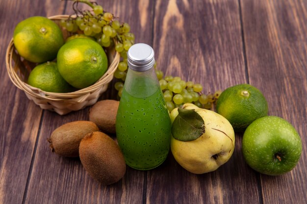 Side view juice bottle with pear kiwi tangerines apples and grapes in a basket on a wooden wall