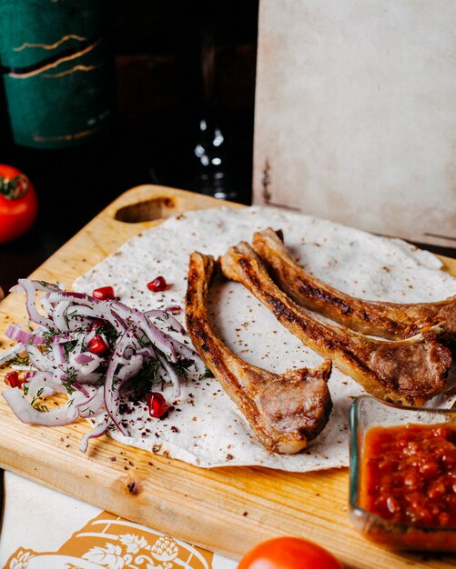 Side view of kebab lamb ribs with red onion and pomegranate on a wooden board