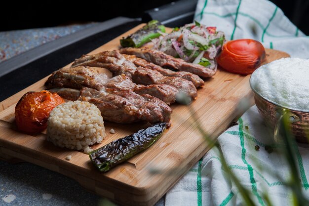 Side view kebab ribs with fried vegetables and chopped onion and ayran and knife in cutting board
