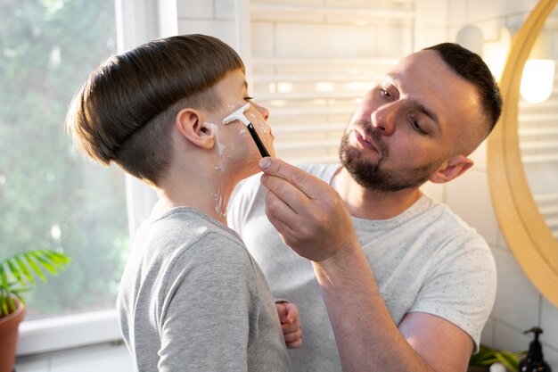 Side view kid learning to shave with father