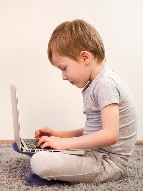 Вид сбоку малыш играет на полу со своим ноутбуком