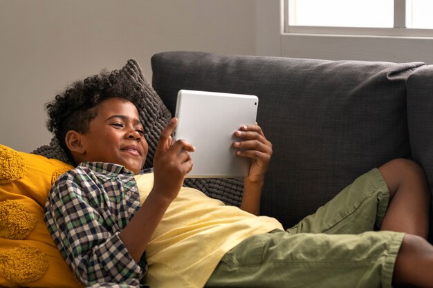 Side View Kid Sitting On Couch With Tablet