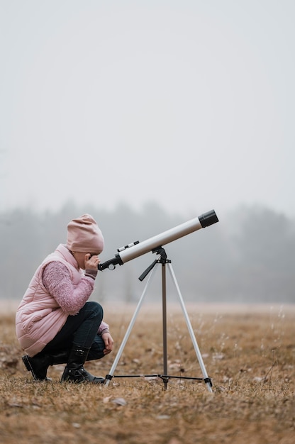Side view kid using a telescope outside
