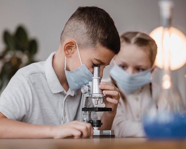 Side view kid with medical mask looking through a microscope