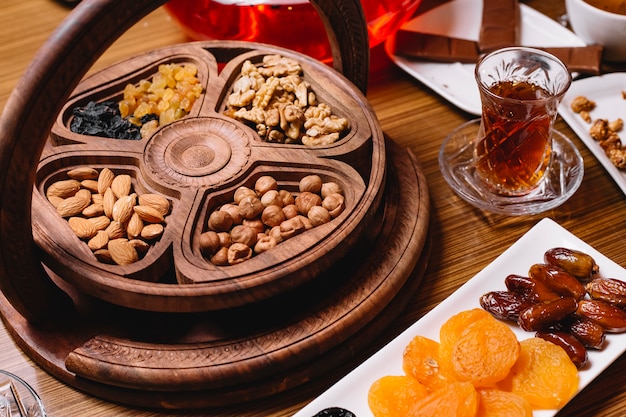 Side view a kind of nuts in a tray with a glass of tea and dried fruits