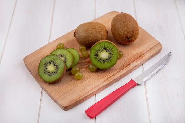 Side view kiwi on a cutting board with a knife on a white wall