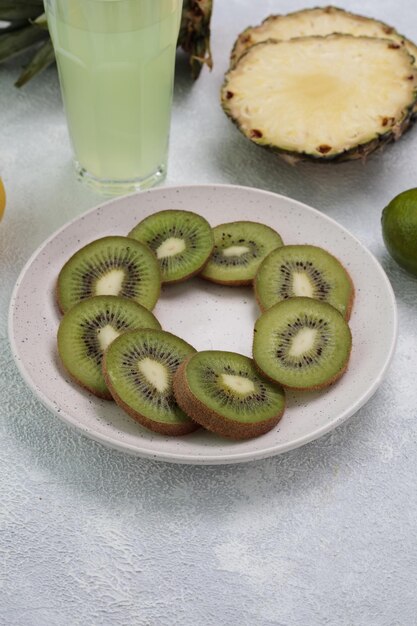 Side view of kiwi slices in plate with lime juice in glass pineapple slices on white background