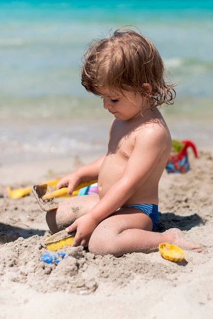 해변에서 모래를 가지고 노는 무릎을 꿇고 아이의 모습